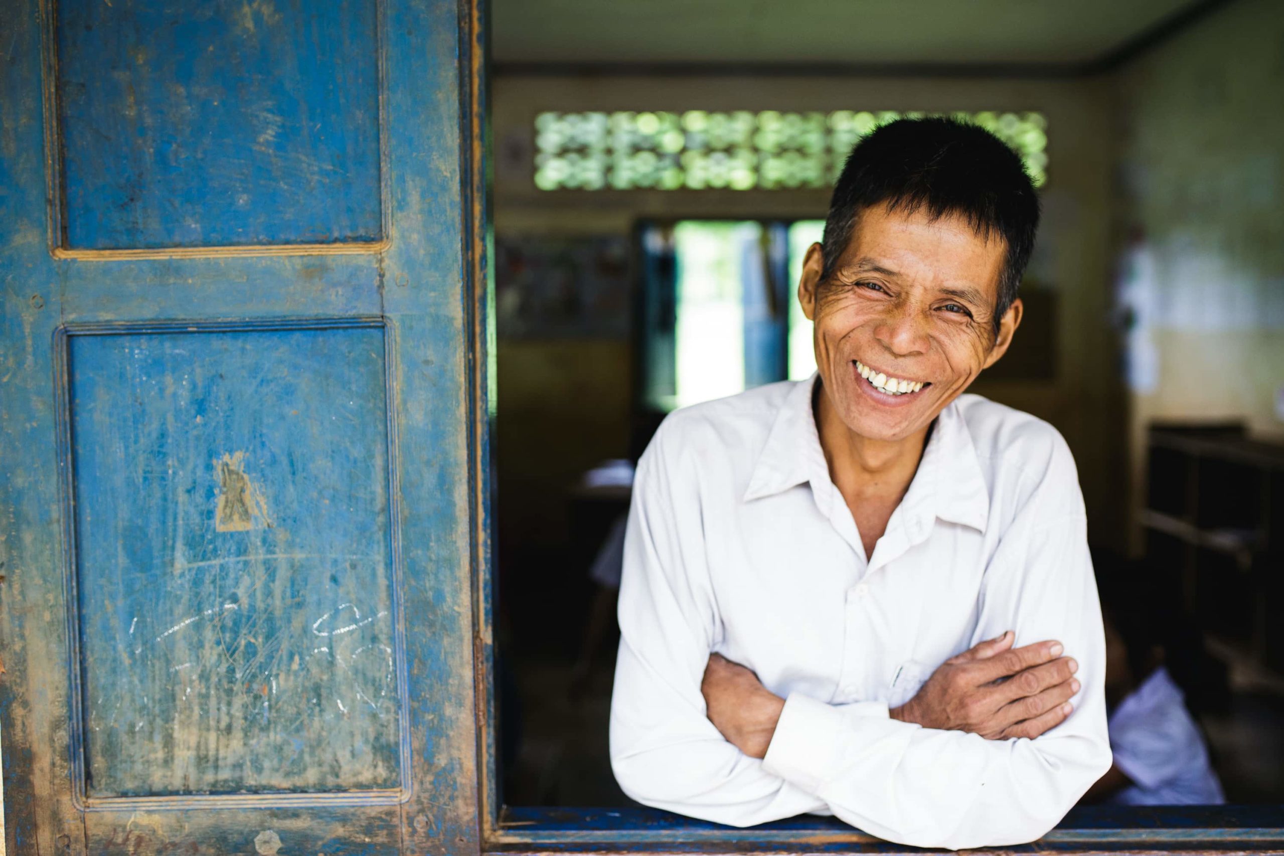 A teacher in Laos looks out of the window of the classroom and smiles.