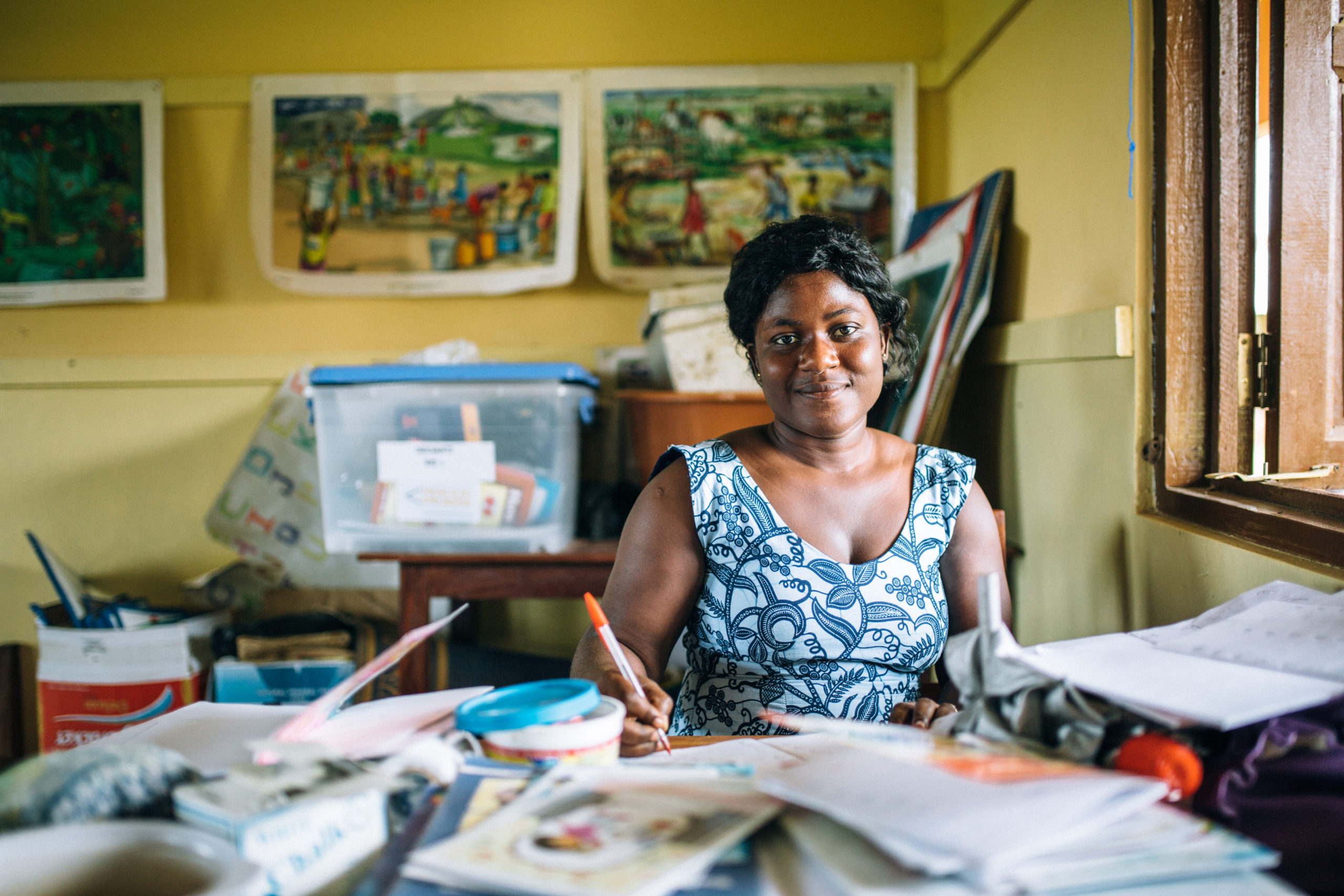 A teacher in Ghana sits at their desk grading papers inside a classroom | Photo credit: Timmy Shivers