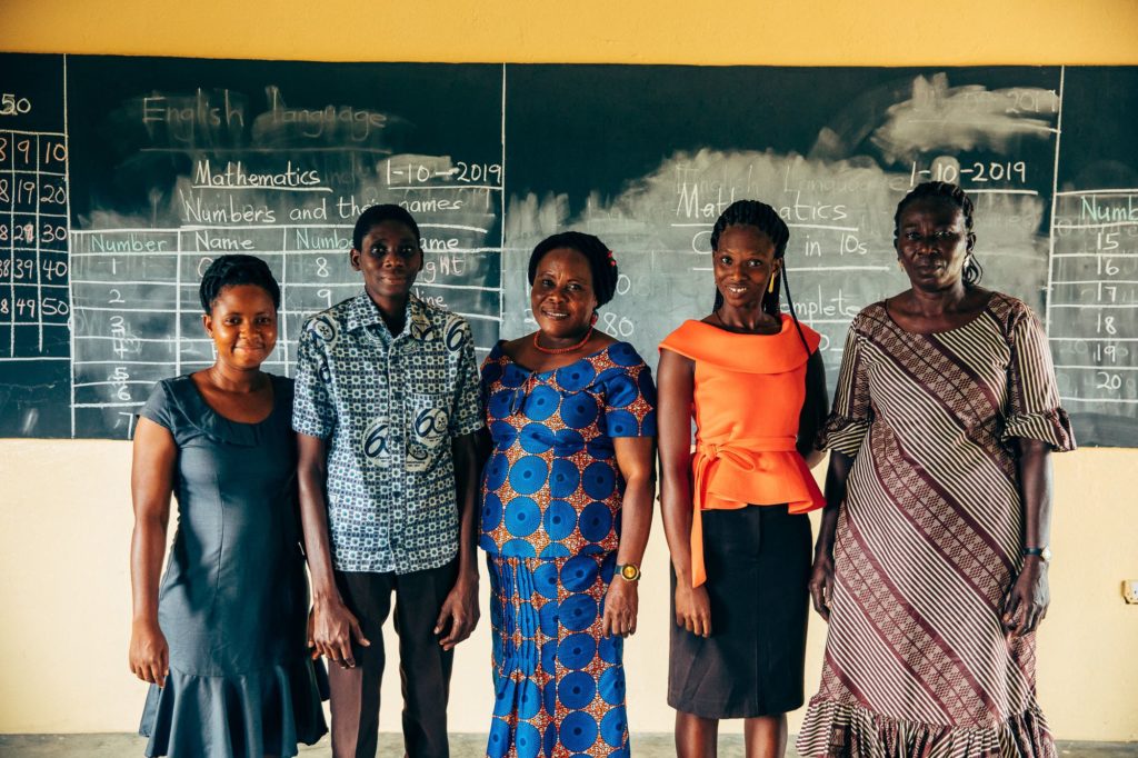 Five teachers in a PoP-supported classroom in Ghana gather in front of the blackboard for a picture.